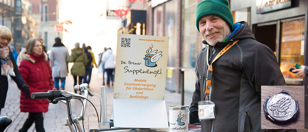 Ein Foto in der Fußgängerzone Bremen/Sögestraße ist im Hintergrund zu sehen. Im Vordergrund rechts ein Mann mit grüner Mütze, grauem Vollbart, schwarzer Jacke und einem Umhängeausweis an orangenem Band. Der Mann lächelt. Links von ihm steht auf einem kaum sichtbaren Lastenrad von uns eine Spendendose mit unserem Logo. Am Lastenrad gut sichtbar ist ein Plakat in DIN A2 befestigt auf dem unsere URL, unser Logo und der Schriftzug "Mobile Essensversorgung für Obdachlose und Bedürftige" zu sehen sind. Rechts unten im Bild ist ein kleiner Ausschnitt eingefügt auf dem eine Plombe mit dem Suppenengel Logo zu sehen ist.